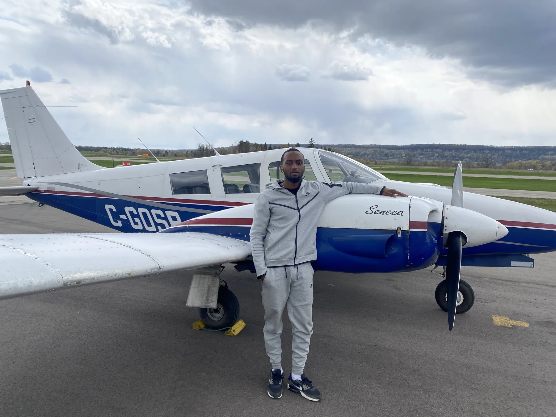 Sam Nyombi beside a Piper Seneca aircraft